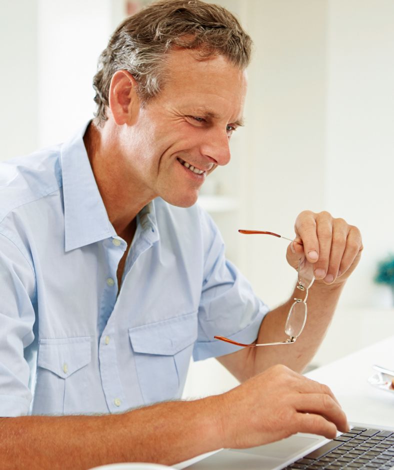 man holding an eye glass while typing on a laptop